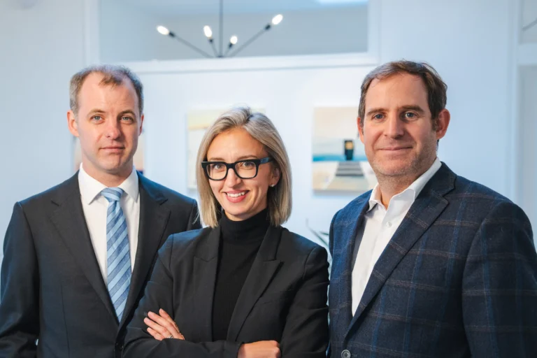 A photo of three lawyers standing in their office at 365 Duckworth Street, St. John's, Canada. Michael Collins on the left, Melissa Saunders in the middle, and Jeremy Loeb on the right. They are smiling warmly and looking at the camera, creating an inviting and professional atmosphere.